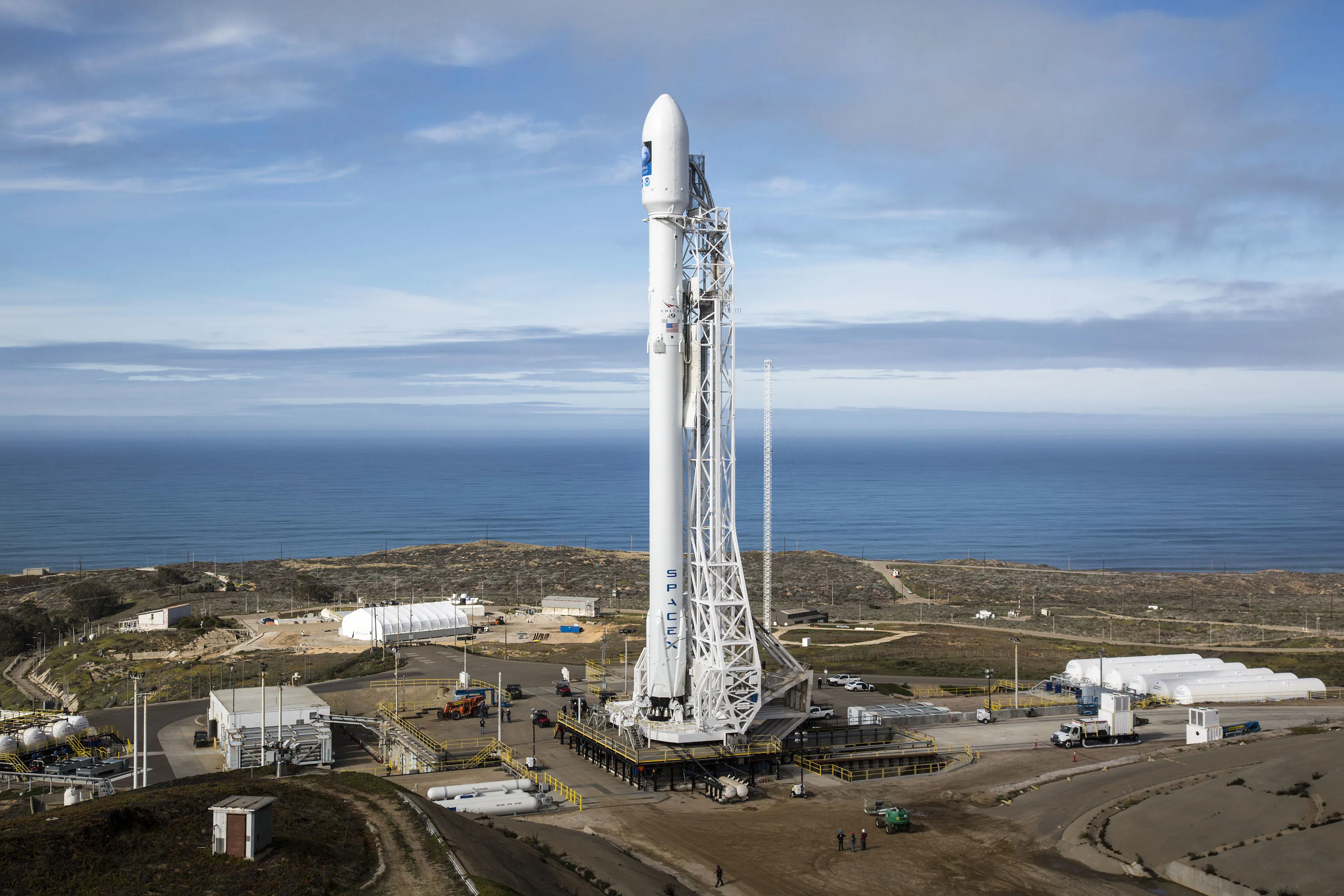 A SpaceX Falcon 9 rocket stands vertical on its launch pad under a clear sky.