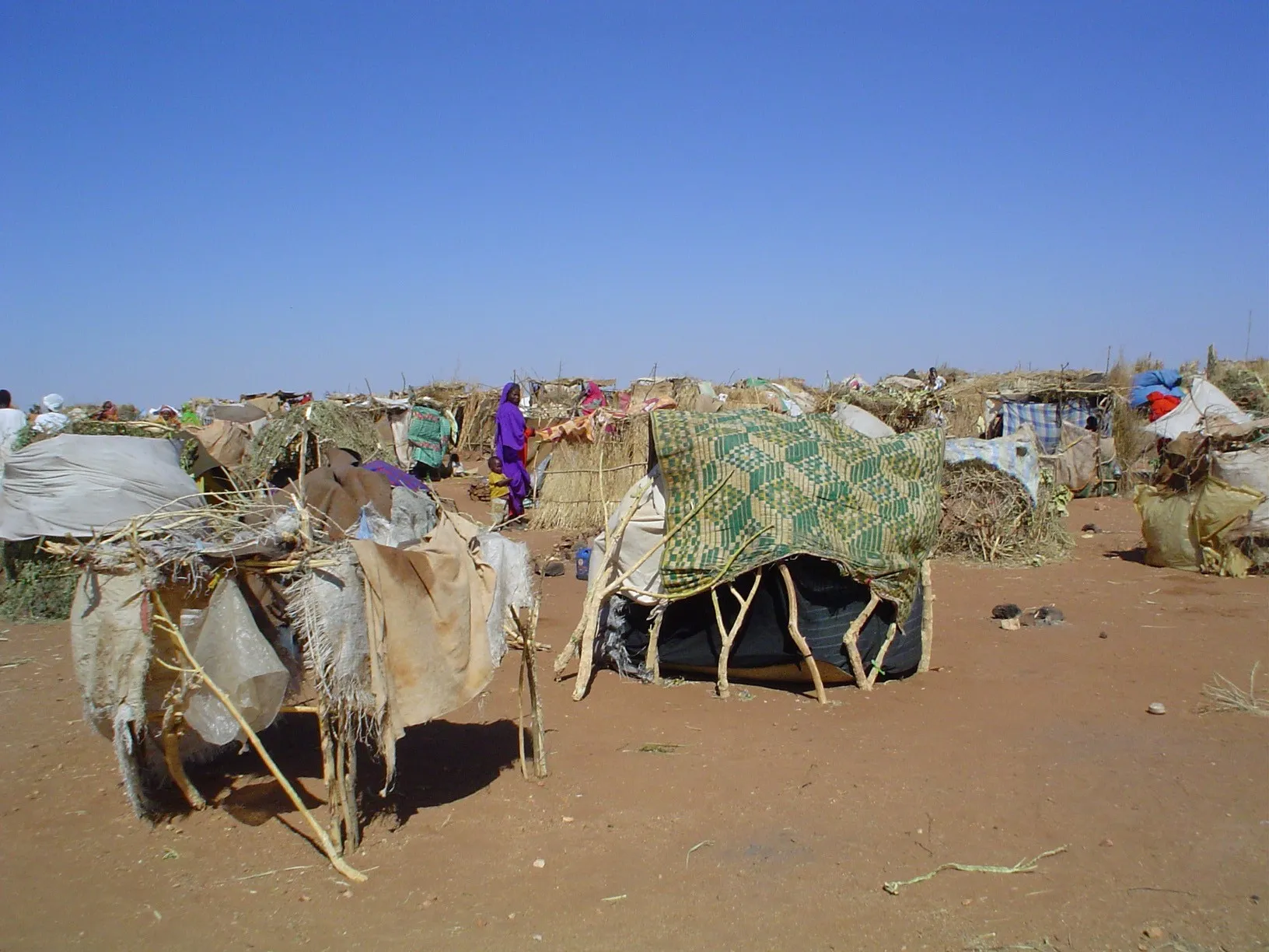 Makeshift shelters built from sticks and plastic sheeting at a camp for people displaced by conflict in Darfur, Sudan.