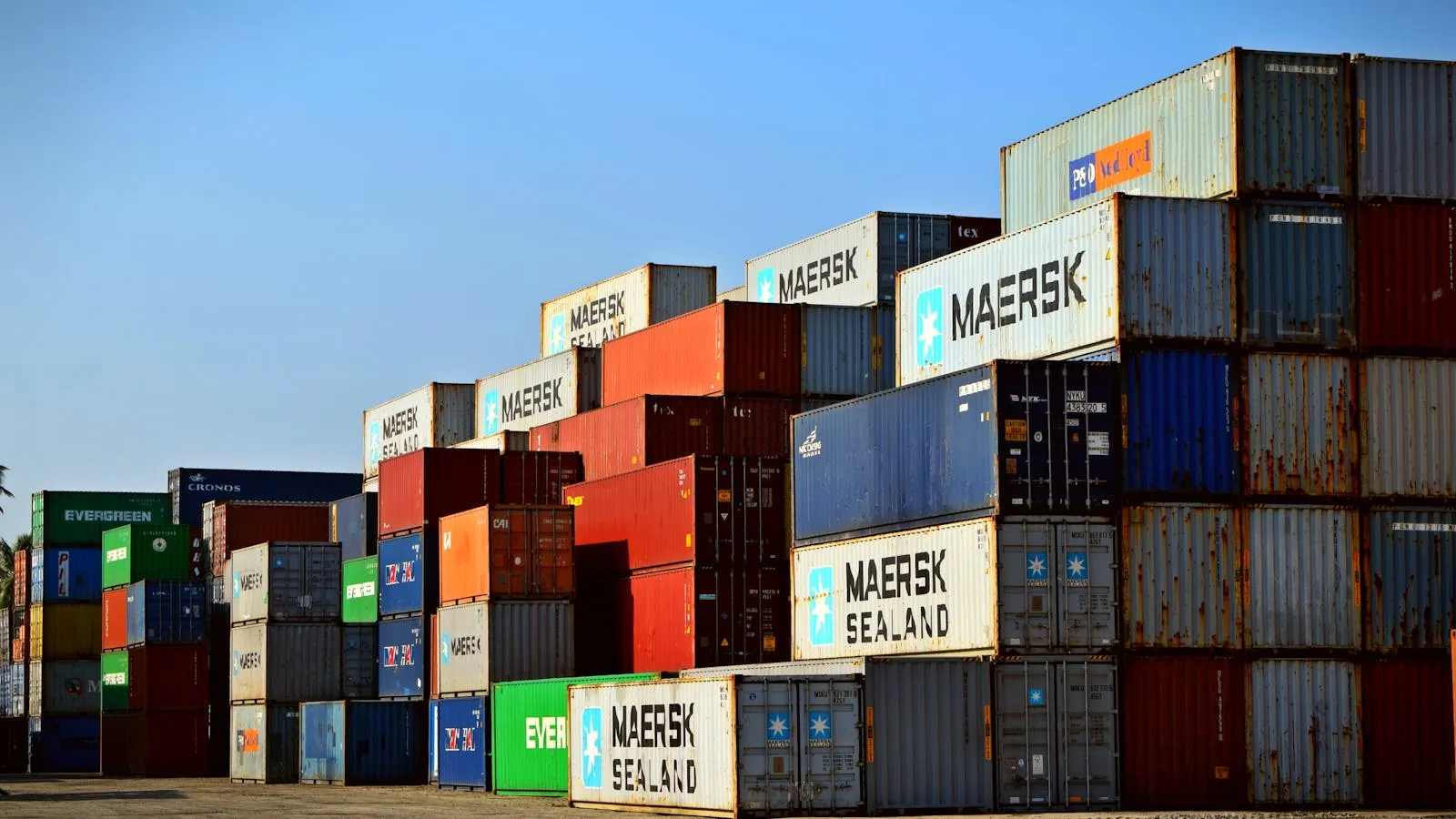 Stacked multicolored shipping containers fill a port terminal under an overcast sky.