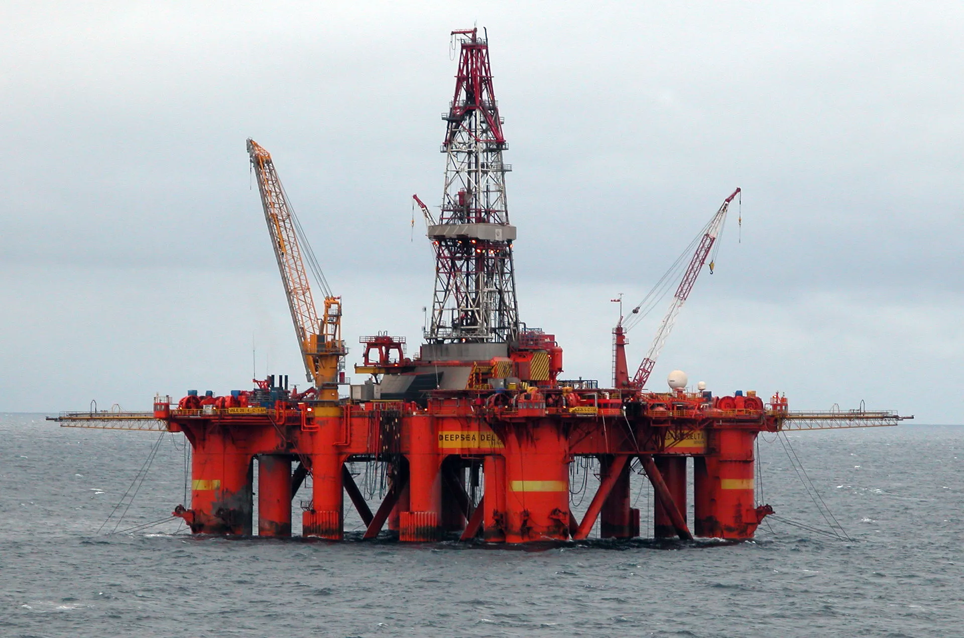 An offshore oil and gas production platform standing above open ocean water under a clear sky.