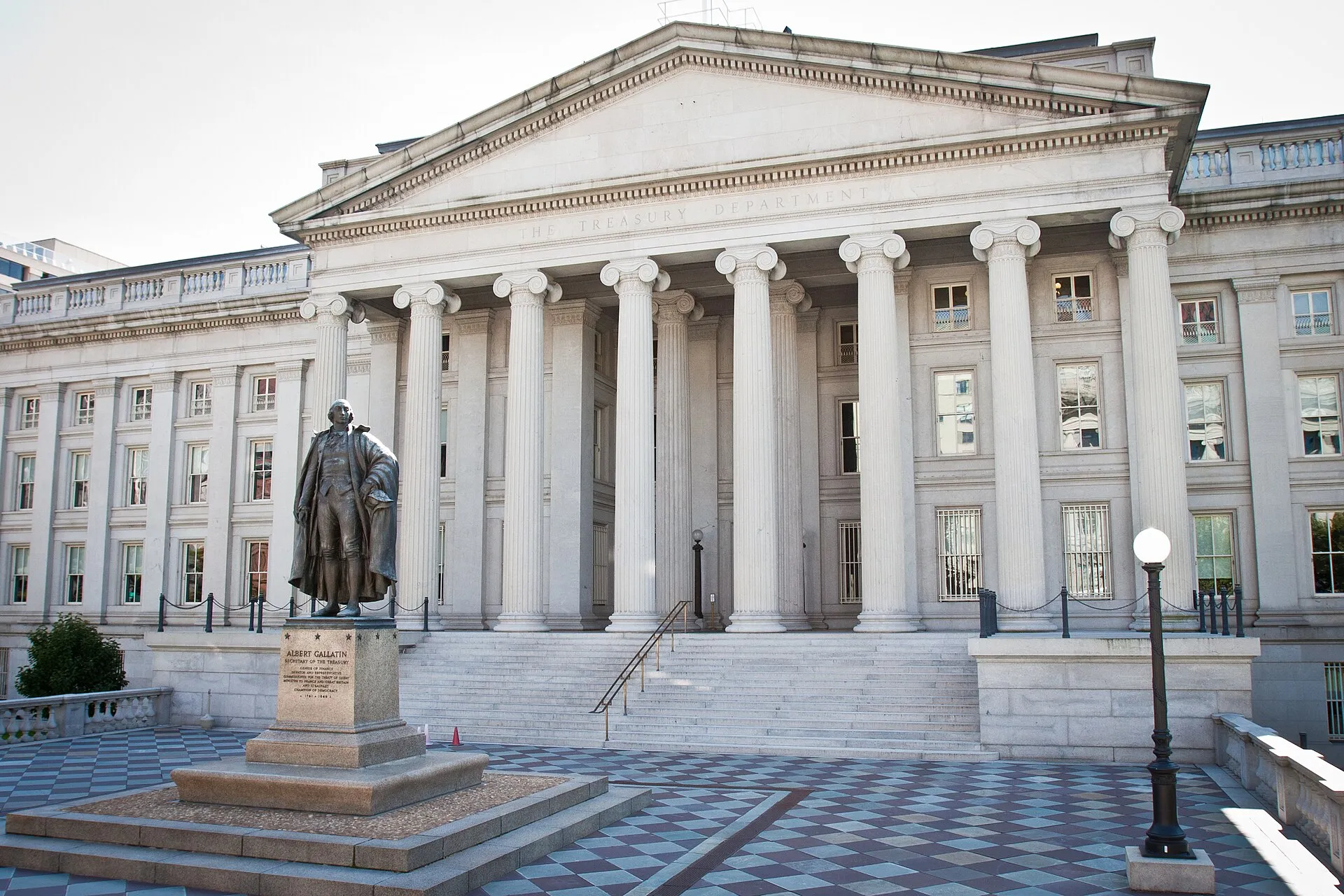 The U.S. Treasury Department building in Washington with its columned facade and a statue of Alexander Hamilton in front.