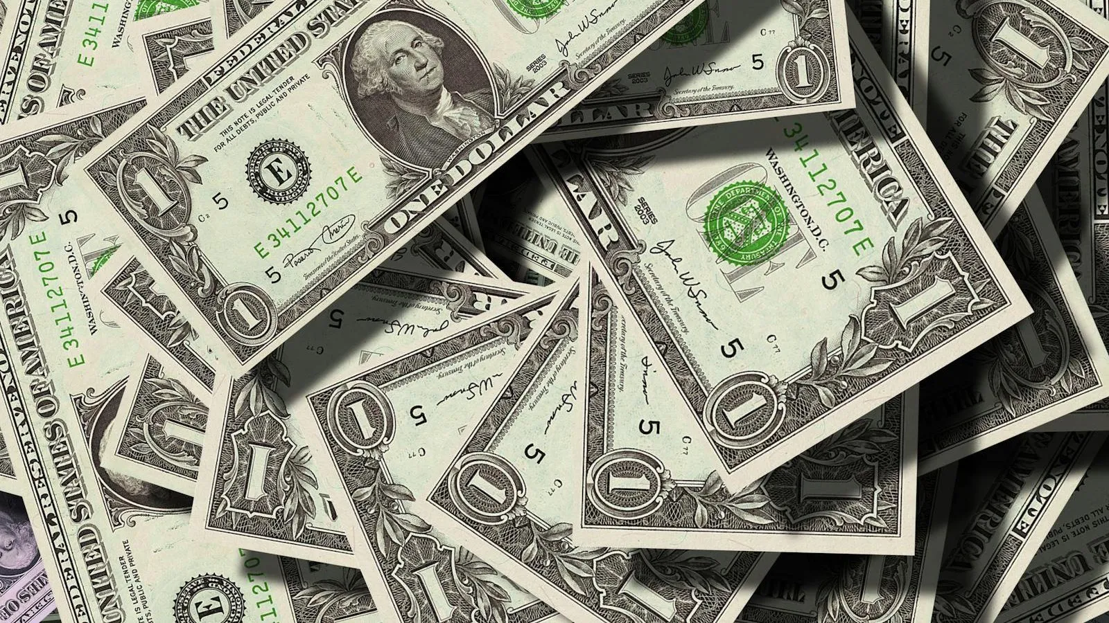A scattered pile of U.S. one-dollar bills showing the portrait of George Washington and the green Treasury seal.