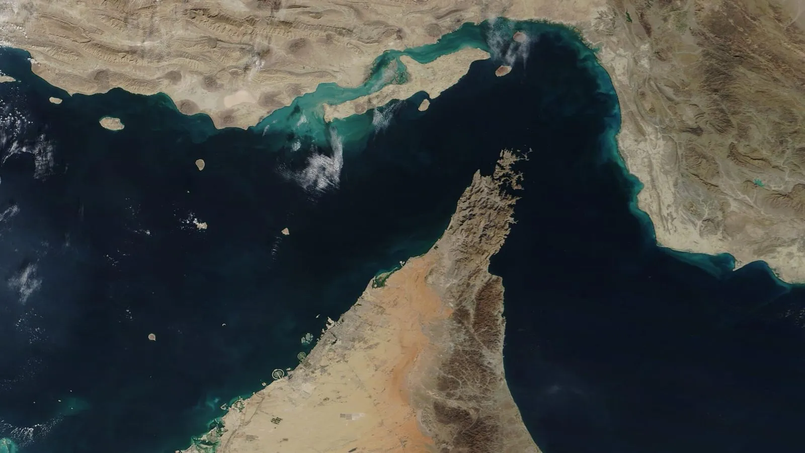 A NASA satellite view of the Strait of Hormuz, with the mountainous coasts of Iran to the north and Oman's Musandam Peninsula to the south framing the narrow blue channel.