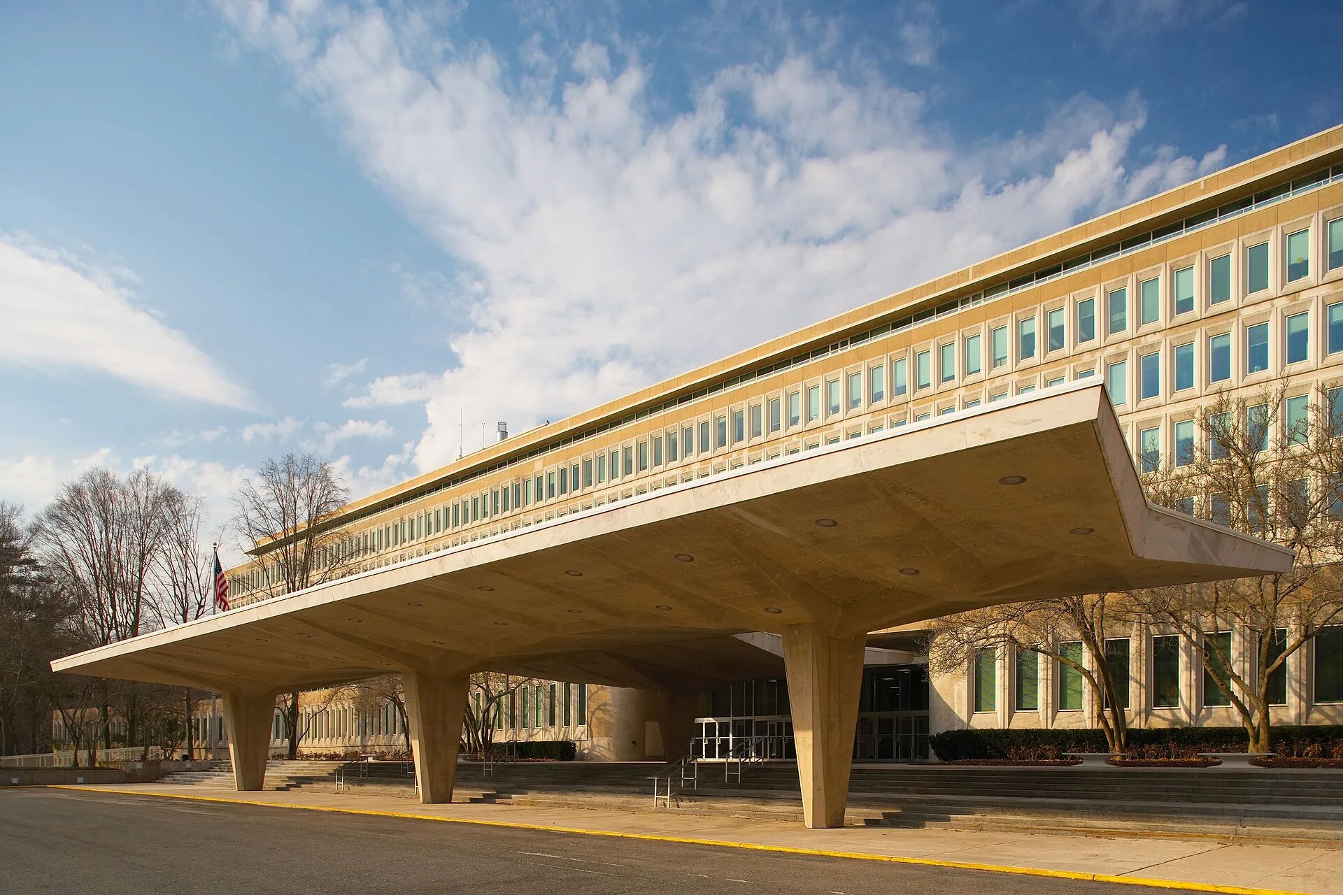 The cantilevered concrete entrance canopy and glass facade of the CIA's Original Headquarters Building under a blue sky.