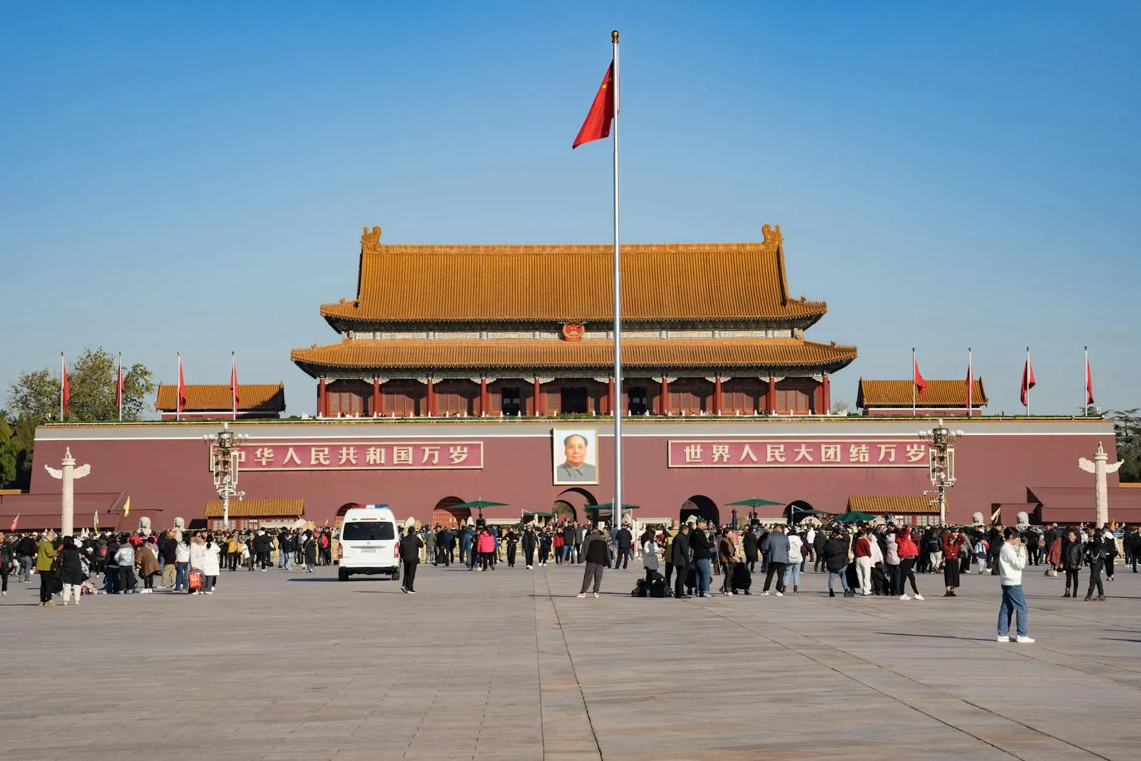 Tiananmen Gate in Beijing, with the Chinese national flag flying above the entrance and crowds of tourists gathered in the square