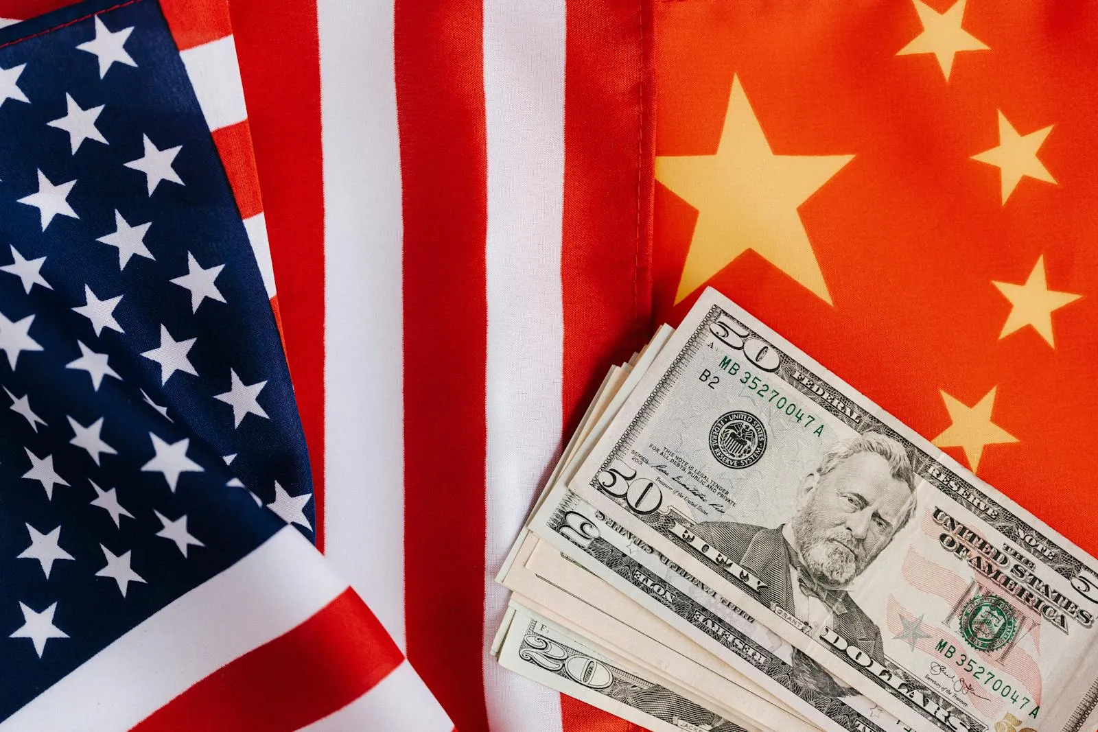 United States dollar bills fanned out across a United States flag and a Chinese national flag, photographed from above on a flat surface
