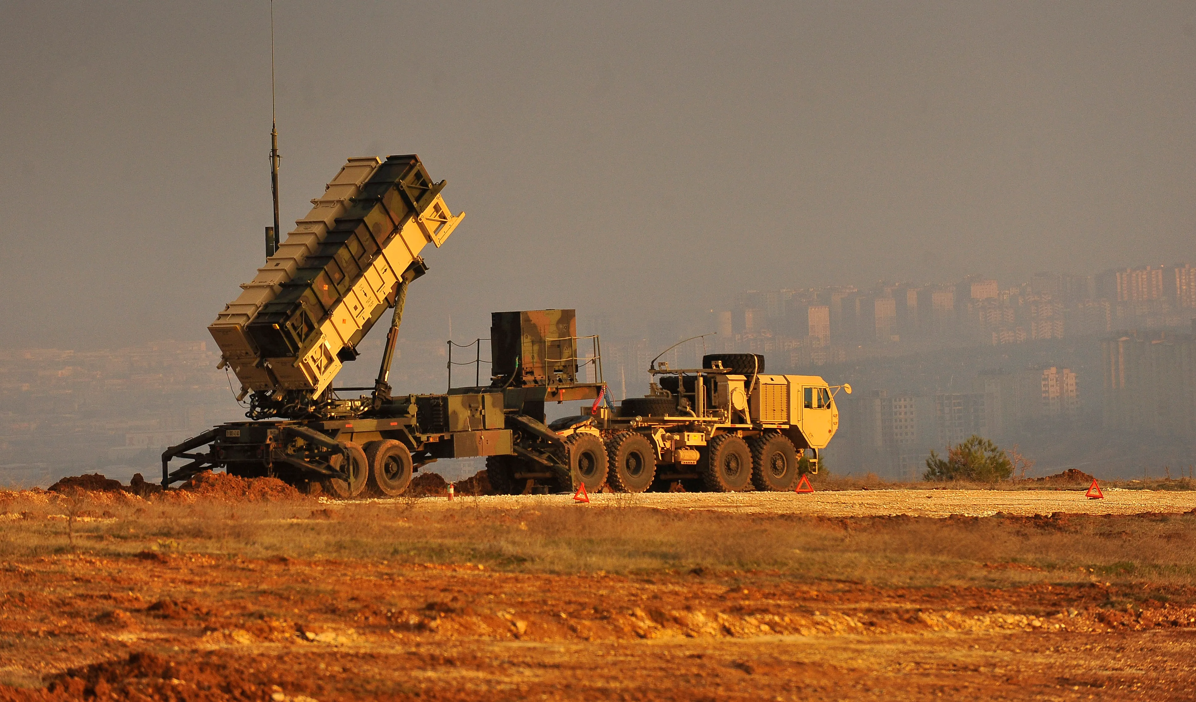 A Patriot missile defense system with white rectangular launch canisters on a hilltop military base overlook