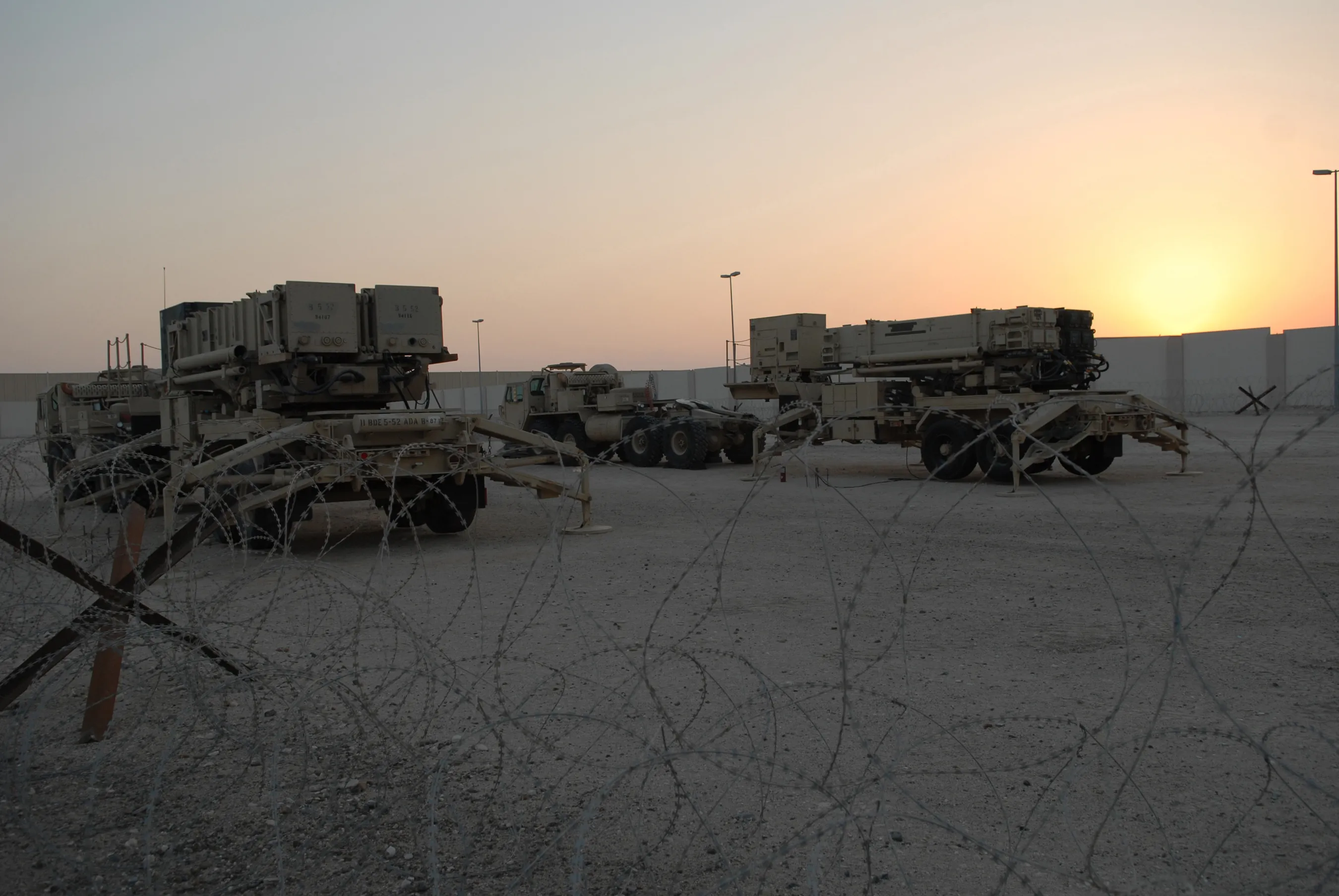 Two Patriot PAC-3 missile launcher vehicles positioned at an air base in Southwest Asia, pointed skyward and ready for deployment