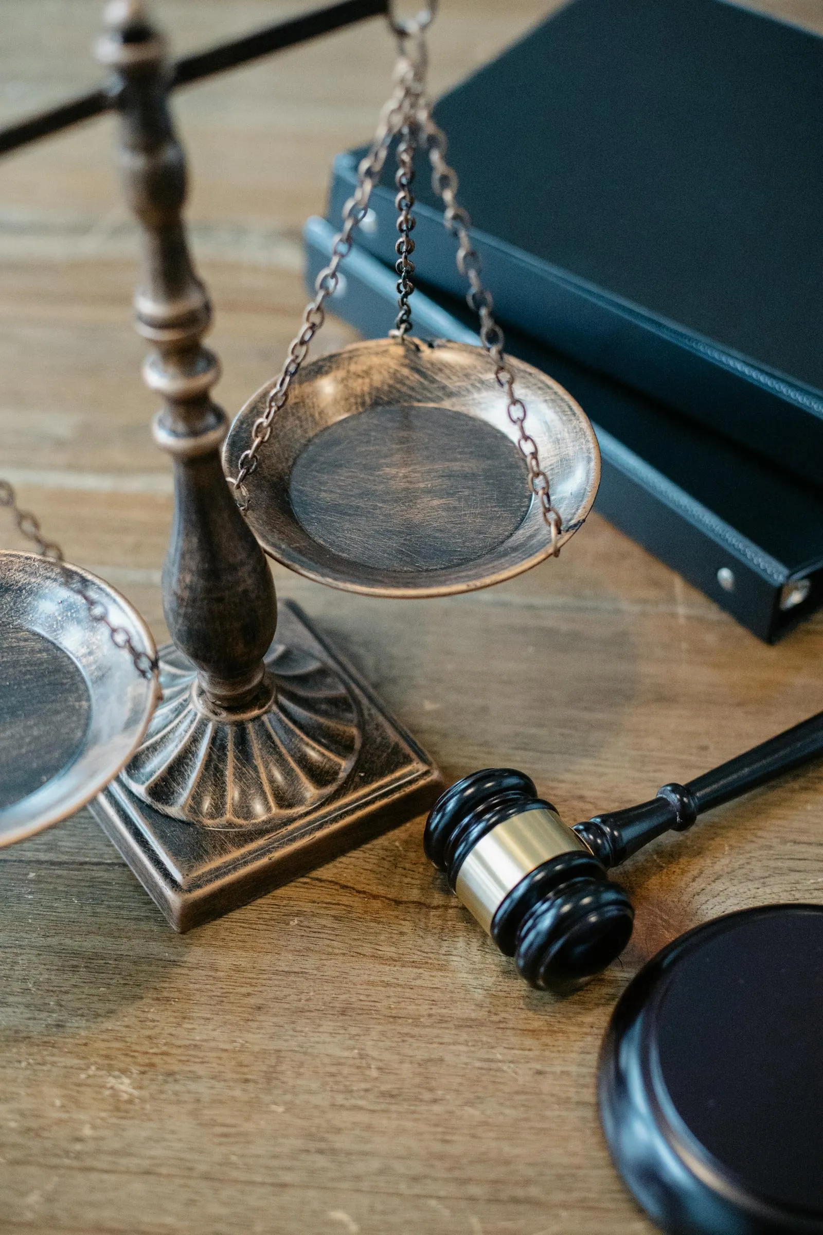 A brass scale of justice balanced on a wooden surface beside a judge's gavel and stacked law books.
