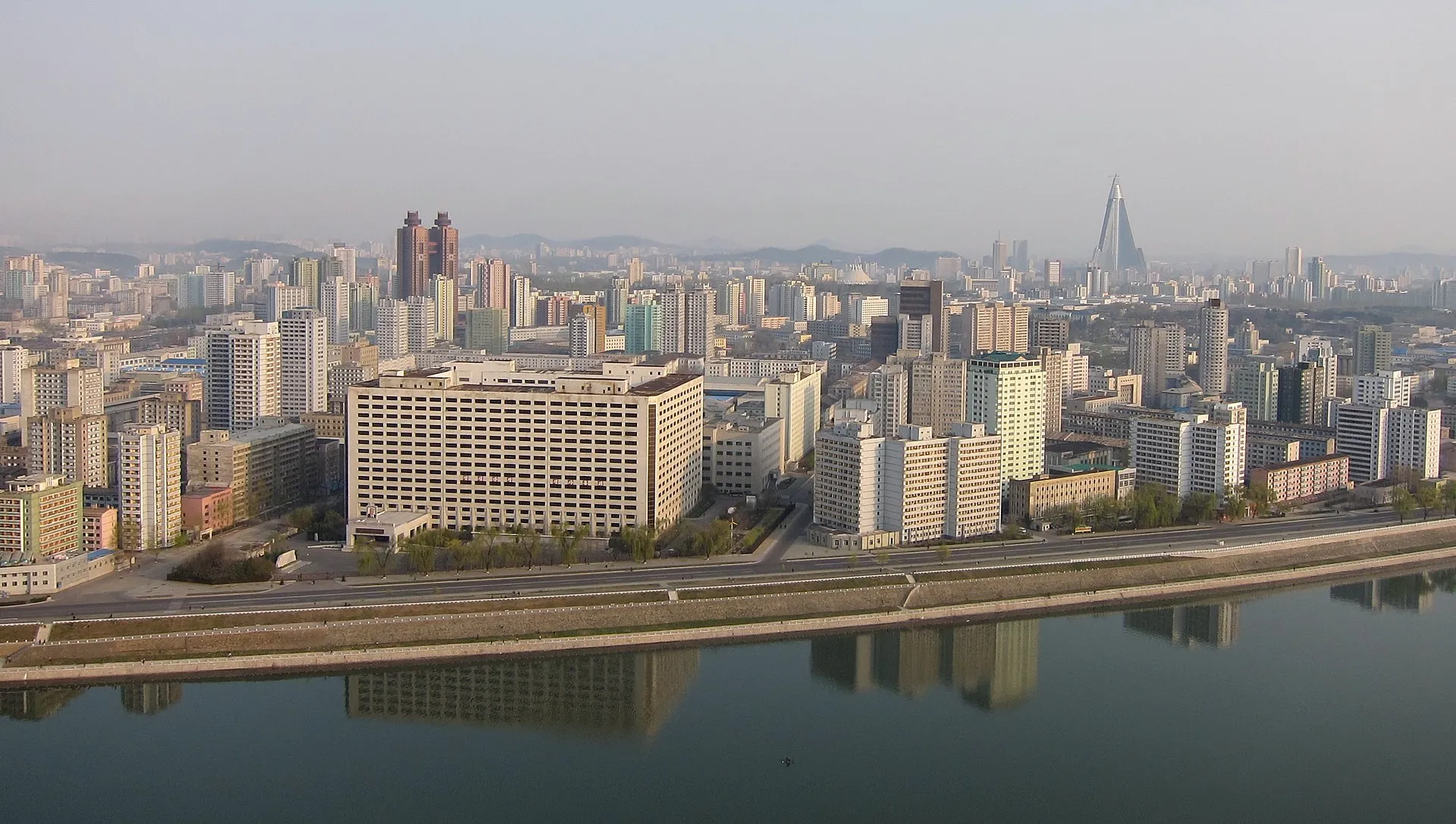 A daytime skyline of Pyongyang, North Korea, showing apartment towers and monuments under a hazy sky.