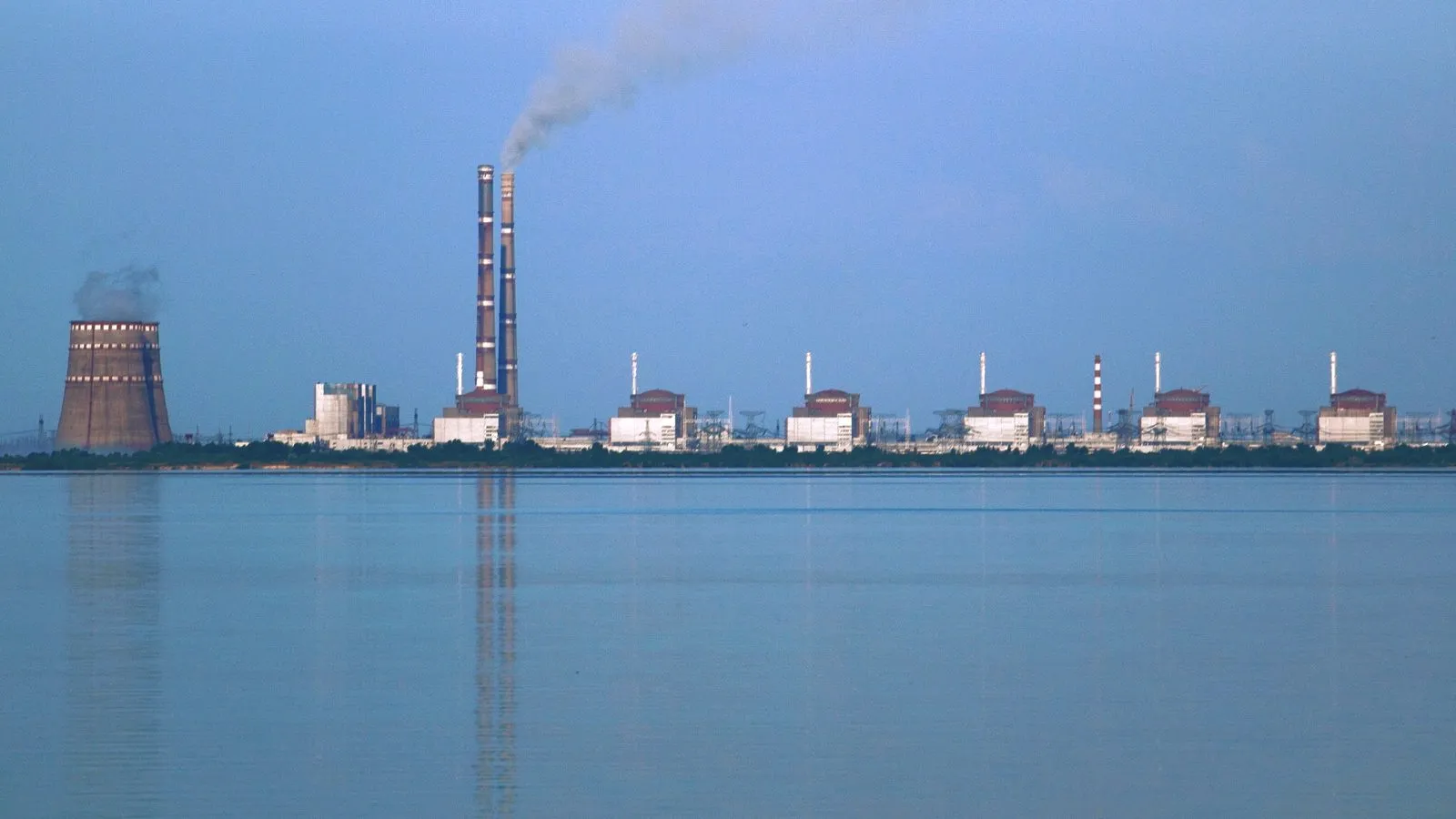 The reactor buildings and cooling infrastructure of the Zaporizhzhia Nuclear Power Plant lined up beside a reservoir, photographed from across the water.